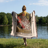 Person holding a tapestry with 'The Empress' design by a lake
