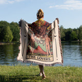 Person holding a Tarot card-themed blanket by a lake