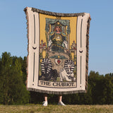 Person holding a 'The Chariot' tarot card blanket outdoors with trees and blue sky in the background
