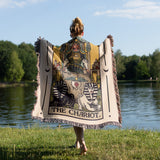 Person holding a Tarot card-themed blanket by a lake