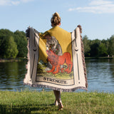 Person walking outdoors with a tarot card-themed blanket draped over them, featuring a lion and the word 'Strength'.