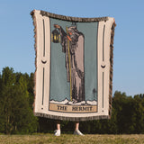 Person holding a tarot card-themed blanket with 'The Hermit' design outdoors.