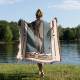 Person holding a tarot card-themed blanket by a lake