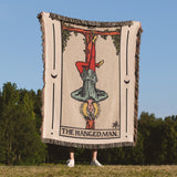 Person holding a woven blanket with 'The Hanged Man' tarot card design outdoors.