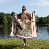Person holding a tarot card-themed blanket with 'Temperance' design by a lake.