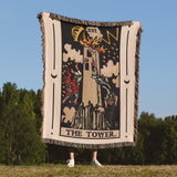 Person holding a tarot card-themed blanket with 'The Tower' design outdoors.