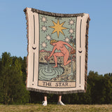 Person holding a 'The Star' tarot card blanket outdoors with trees and blue sky in the background