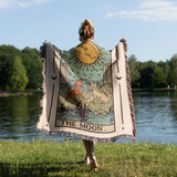 Person holding a tarot-themed blanket by a lake