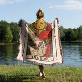 Person holding a tarot card-themed blanket by a lake