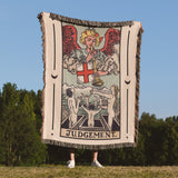 Person holding a tarot card-style blanket with 'Judgment' design outdoors.