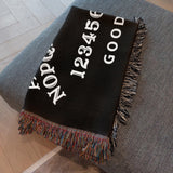 Black Ouija blanket with white text and numbers draped over a gray couch.