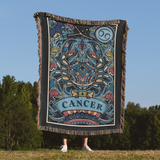 Person holding a decorative blanket with 'Cancer' design against a natural background