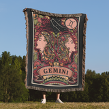 Person holding a 'Gemini' themed blanket with astrological design outdoors.