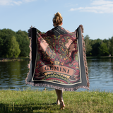 Person holding a 'Gemini' themed blanket by a lake