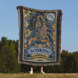 Person holding a decorative blanket with Scorpio zodiac design against a natural background
