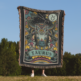 Person holding a Taurus-themed blanket with astrological design outdoors.