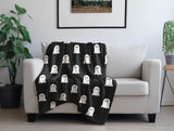 Black blanket with white ghost patterns draped over a white armchair in a room with plants and a framed picture.
